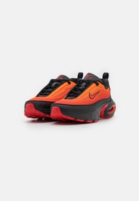 Nike sportcipők, piros és narancssárga felsőrésszel, fekete részletekkel, vastag talppal és texturált felülettel, a kényelem és a stílus jegyében tervezve.