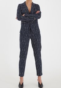 Traje azul marino con un patrón de rayas finas de líneas verticales blancas. La americana tiene solapas de muesca y se combina con pantalones de corte ajustado.