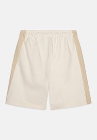 Pantalones cortos de algodón crema con un panel lateral beige, cinturilla elástica y una textura suave. No hay bolsillos visibles en el diseño.