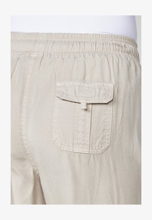 Beige cargo bukser har en baglomme med klap, elastisk talje og tekstureret stof, hvilket fremhæver et praktisk og afdæmpet design.