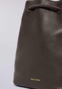 Brun læderbucket-taske med en glat tekstur, med snor-lukning og et gyldent "Trussardi"-logo nederst.