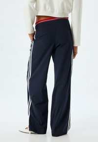 Pantalones de rayas marineras con franjas laterales blancas y una cinturilla en contraste rojo y blanco. Confeccionados en una suave tela texturizada; corte holgado.