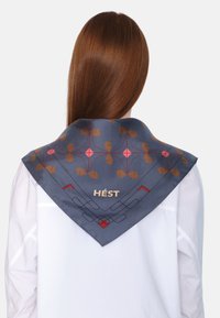 Silk kvadratisk skjerf, marineblått med geometriske og blomster mønstre i brunt og rødt, med teksten "HÉST" i gull nær bunnen av kanten.