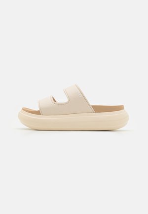 Kremfargede sandaler med tykk, strukturert såle. Har doble, brede stropper og en glatt såle. Logo vises på stroppen.