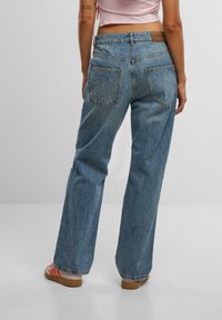 Light blue denim jeans with a relaxed fit, high waist, two back pockets, and visible stitching details, paired with brown sandals.