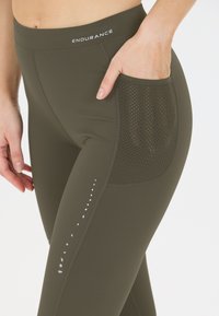 Stretchiga olivgröna träningsleggings med en texturerad meshficka, reflekterande prickmönster på sidan och en elastisk midja.