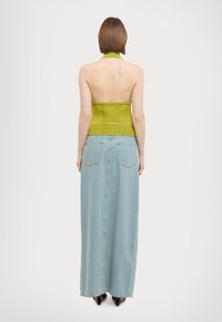 Zelený halter-top s přiléhavým korzetem, kombinovaný s dlouhou světle modrou džínovou sukní, která má zadní kapsy a rovný střih.