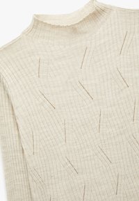 Beige gebreide trui met een hoge kraag en geribbelde textuur. Bevat verticale lijnen en uitsnijdingen doorheen de stof.