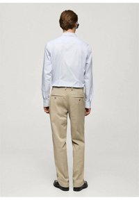 Lichtblauwe overhemd met lange mouwen en knopenmanchetten, in combinatie met beige broeken met zakken. De outfit wordt compleet gemaakt met zwarte schoenen.