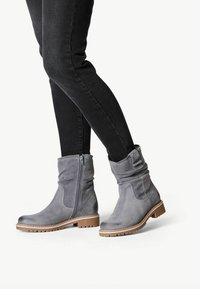 Bottines en daim gris avec une fermeture éclair sur le côté, au design bavard, et une semelle beige robuste. Assorties à un jean foncé pour créer un contraste.