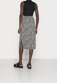 Czarny top bez rękawów w połączeniu z białą i czarną spódnicą do kolan z wzorem i bocznym rozcięciem. Modelka nosi czarne sandały.