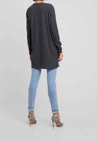 Grå ribbad långärm topp med sidoflikar, tillsammans med ljusblå smala jeans och beige högklackade skor med ormskinnsmönster.