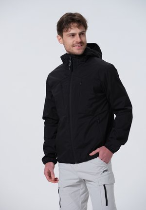 Schwarze wasserdichte Jacke mit Reißverschluss, elastischen Ärmelbündchen und zwei Brusttaschen, getragen mit hellen Cargo-Hosen.