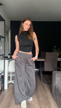 Black sleeveless top paired with gray pinstriped wide-leg trousers. The outfit features side pockets and light-colored footwear.
