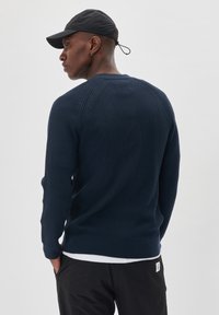 Navy ribbed knitted sweater with long sleeves, featuring a round neckline and a textured finish, worn over a white shirt.