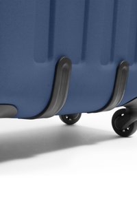 Blue hard-shell suitcase with textured surface, curved black plastic accents, and four black wheels at the base for mobility.