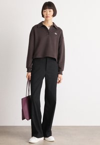 Brown cropped sweatshirt with a collar and button placket, paired with black wide-leg trousers and white sneakers. Model carries a purple bag.