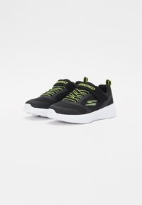 Zapatillas deportivas negras con parte superior de malla, cordones verde neón y suela blanca. Cuenta con una correa de Velcro y detalles texturizados.