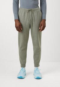 Light green, cotton blend joggers with elastic waistband, drawstring, and fitted cuffs. Worn with light blue athletic shoes.