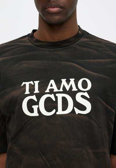 Svart t-skjorte laget av bomull, med hvit tekst "TI AMO GCDS." Stoffet har en litt teksturert, falmet utseende.