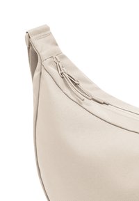 Béžová textilná taška s hladkou textúrou, zakriveným tvarom a zipsom, s dekoratívnym detailom šnúrky na jednej strane.