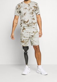 Conjunto de camuflaje gris claro que incluye una camisa de manga corta y pantalones cortos, con una textura suave y una pierna prostética negra.