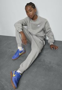 Hallide hallide Nike tolm ja püksid, millel on väike logo. Sinised ja kollased Nike tossud kummipõhjaga, paigutatud hallile pinnale.