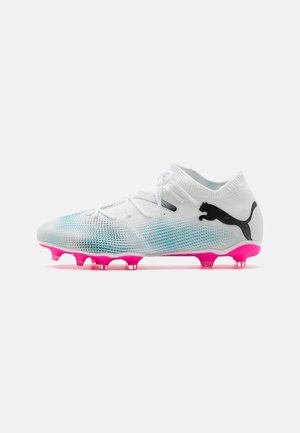 Botas de fútbol blancas con un diseño de tobillo de punto, patrón en degradado azul, logo negro y suela rosa con seis clavos para tracción.