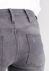 Šedé džínsy z denimu s fitted střihem, středně vysokým pasem, dvěma zadními kapsami a jemnými poškozeními na textuře látky.