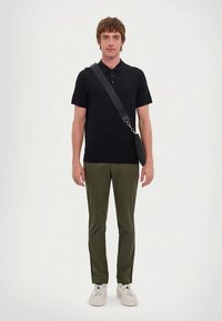 Černé polo tričko, olivově zelené kalhoty a bílé tenisky. Doplňky zahrnují kabelku přes rameno s černým popruhem. Jednoduchý, moderní střih.