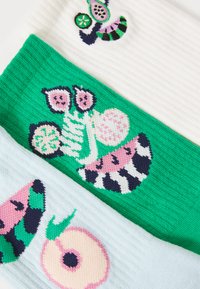 Três pares de meias coloridas: em cima creme com canelado, no meio verde com desenhos de frutas, em baixo azul claro com padrão de frutas cor-de-rosa.