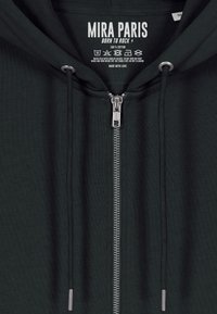 Sötétzöld pamut kapucnis pulóver teljes hosszúságú cipzárral, ezüstszínű cipzárral, állítható húzózsinórral és nyakrészen nyomtatott címkével.