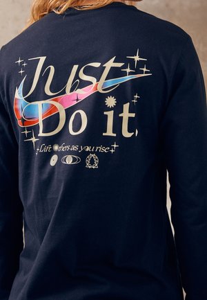 T-shirt à manches longues bleu marine avec un motif coloré "Just Do It" et des étoiles. Le texte inclut "Soulevez les autres en montant," imprimé dans différents styles.