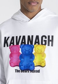 Sudadera blanca con un gráfico de tres personajes de ositos de goma en rosa, azul y amarillo, con el texto "KAVANAGH" arriba y "El escuadrón de ositos" abajo.