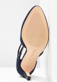 Chaussure à talon bleu marine à bout pointu avec semelle présentant un motif de bande de roulement en forme de vague et nom de la marque "Pier One" en taille 37.