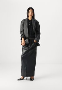 Svart skinn maxiskjørt med høy splitt, kombinert med en mørk teksturert bluse og en grå stripete blazer. Sorte hæler og en svart veske.