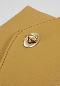 Żółta, teksturowana kopertówka ze skóry z złotym zatrzaskiem i zakrzywioną klapką, z przeszyciami wzdłuż krawędzi.