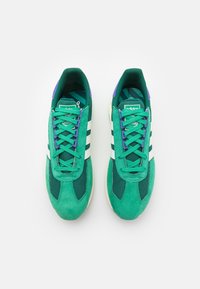 Gröna mocka- och mesh-sneakers med vita ränder och lila detaljer. Har flata snören och en texturerad sula för bra grepp.