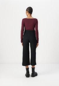 Top de manga larga color burdeos combinado con pantalones acampanados de canalé negros y botas negras de tacón grueso, con cintura alta y diseño texturizado.