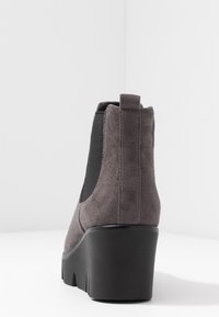 Bottine en suede gris avec des panneaux élastiques noirs sur les côtés et une semelle plateforme épaisse. Le talon présente un dos arrondi et une surface texturée.