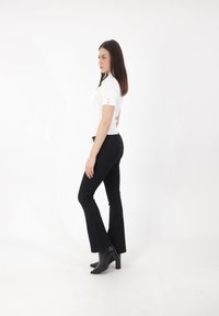 Top corto a maniche corte bianco con dettagli in bottone dorato, abbinato a pantaloni neri a palazzo e stivali neri con tacco, su sfondo bianco.
