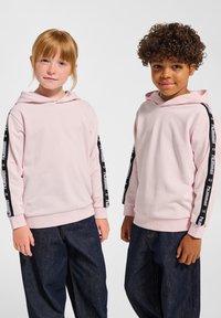 Lichtroze hoodies met zwarte zijkanten voorzien van logo-tekst, gecombineerd met losse donkere denimspijkerbroeken. Zacht, gestructureerd materiaal, casual pasvorm.