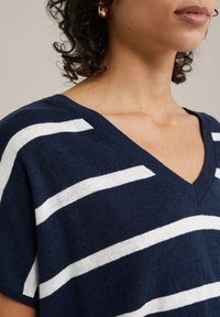 Marinblå V-ringad tröja med vita horisontella ränder, gjord av strukturerad stickad tyg. Har avslappnad passform och korta ärmar.