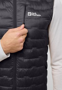 Schwarze, puffige Weste mit gestepptem Muster. Verfügt über eine Reißverschlusstasche auf der Brust und ein Logo auf der oberen linken Seite. Glattes Material.