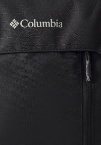 Crni ruksak od tkanine s geometrijskom teksturom, prednjim zatvaračem i srebrnim "Columbia" logotipom na vrhu. Izdržljiv i funkcionalan dizajn.