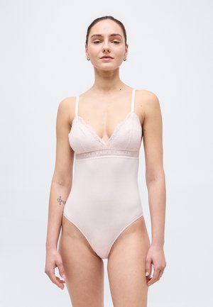 Femme aux cheveux tirés en arrière portant un body rose clair orné de dentelle avec de fines bretelles et le texte "Polo Ralph Lauren" sur la bande.