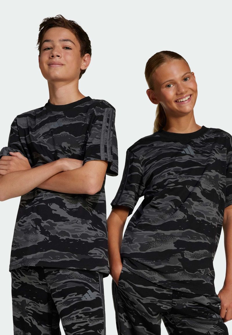 Camisetas deportivas de patrones de camuflaje negro y gris con mangas cortas, que presentan rayas contrastantes en los hombros y un ajuste relajado.