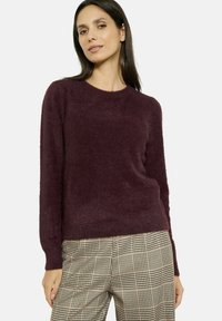 Maglione borgogna peloso con maniche lunghe e colletto a costine, abbinato a pantaloni a quadri a vita alta in beige e nero.