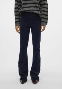 Pantalons en velours côtelé bleu marine évasés avec une texture lisse et une taille ajustée, assortis d'un pull-over rayé gris.
