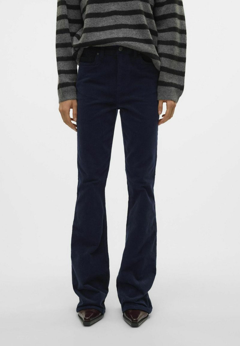 Pantalons en velours côtelé bleu marine évasés avec une texture lisse et une taille ajustée, assortis d'un pull-over rayé gris.